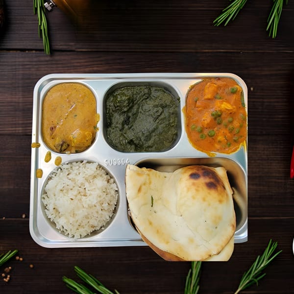 An Indian thali with rice, naan, paneer curry, spinach, and another curry on a wooden table.