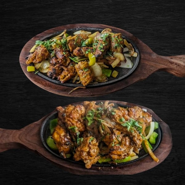 Two sizzling platters of Afghan chicken tikka with onions, peppers, and cilantro on wooden boards.