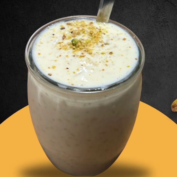 A glass of creamy Afghan drink, topped with crushed pistachios and a spoon.