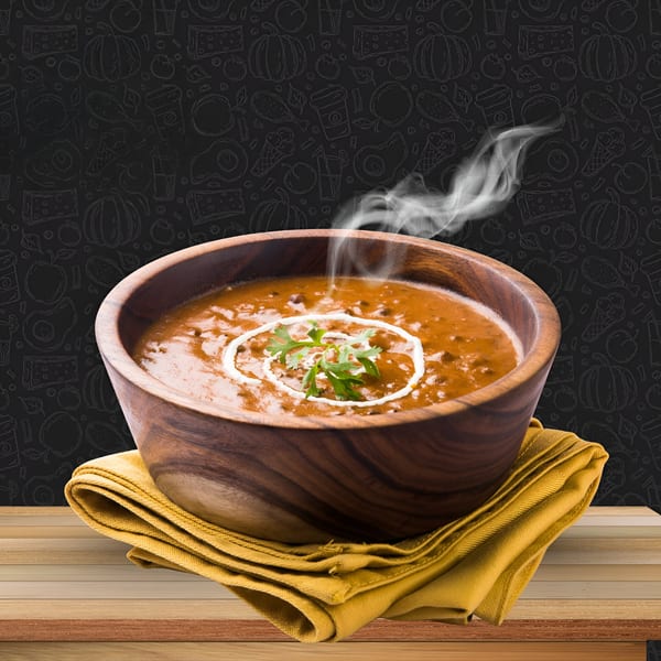 Steaming bowl of King Restaurant's Afghan Dal Makhani, garnished with cream and cilantro, on a wooden table.