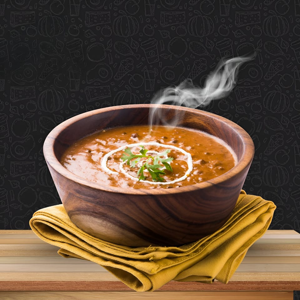 Steaming bowl of King Restaurant's Afghan Dal Makhani, garnished with cream and cilantro, on a wooden table.
