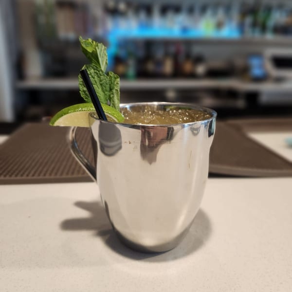 A silver mug cocktail with mint, lime, and a black straw on a white counter.