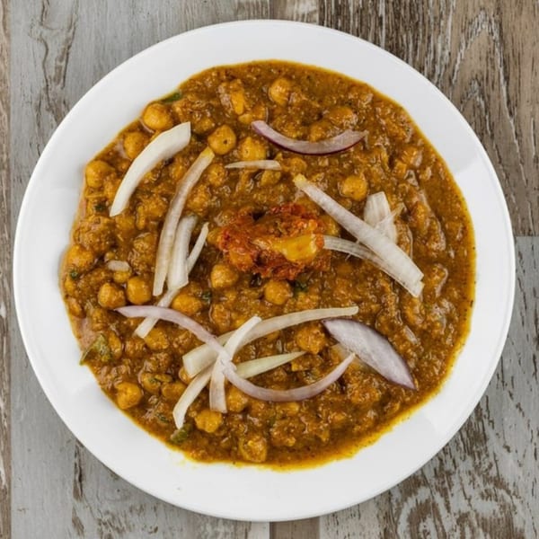 A white plate of Afghan chana masala, garnished with sliced onions and a dollop of red spice.