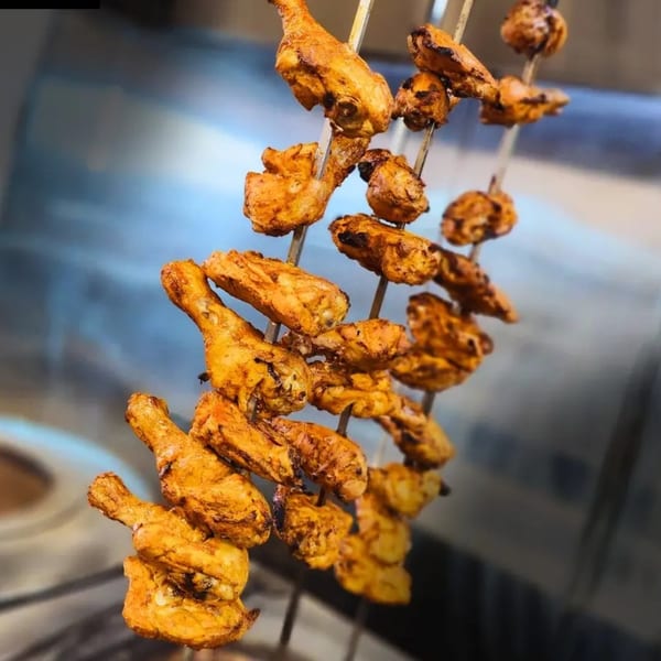 Several skewers of golden-brown, marinated chicken pieces hang vertically, ready for cooking.